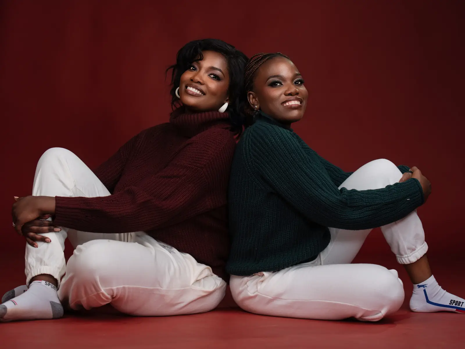 Two friends sitting back to back in a red studio set